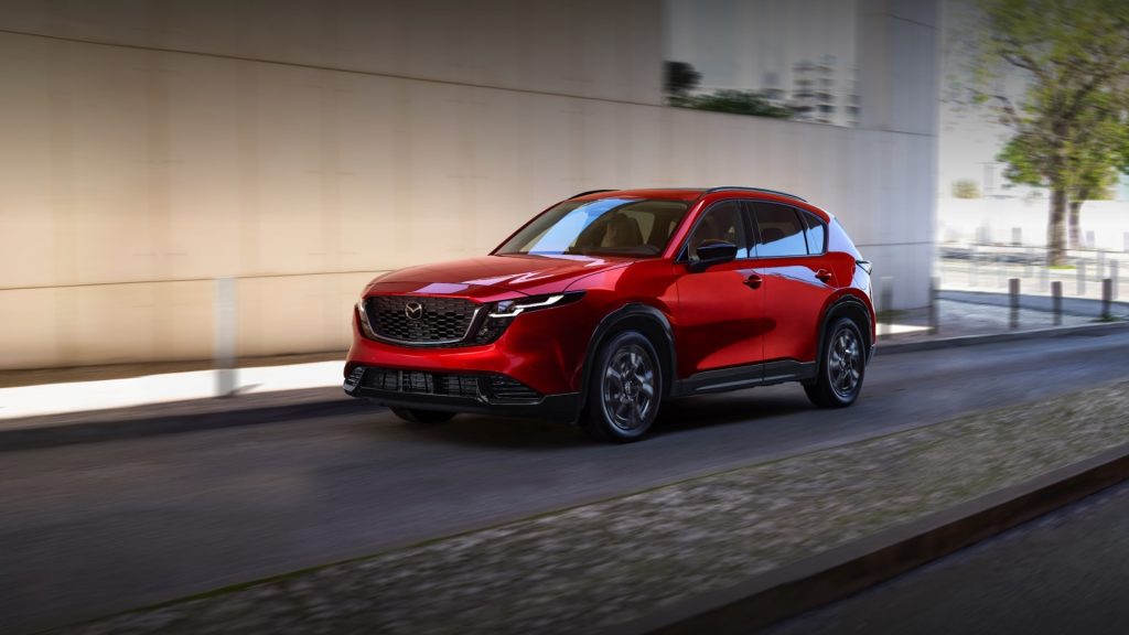 A red Mazda CX-5 driving on a city street, showcasing its stylish and dynamic design with a modern urban backdrop.