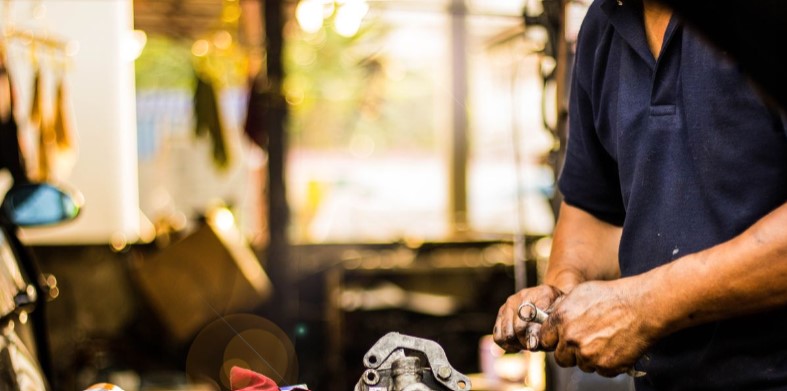 A mechanic working with tools in a well-lit auto repair shop, focusing on adjusting a car part with precision.