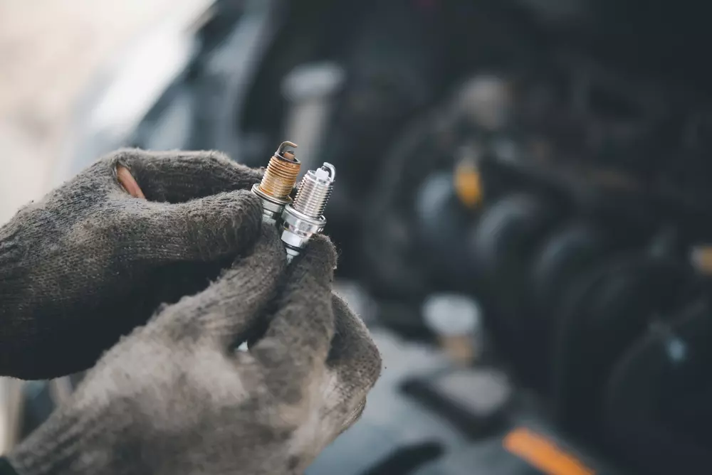 Mechanic comparing worn and new spark plugs during vehicle maintenance